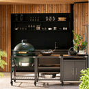 Outdoor kitchen setup with a large green grill and various cooking utensils on a wooden deck.