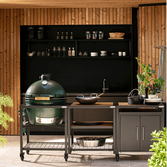 Outdoor kitchen setup with a large green grill and various cooking utensils on a wooden deck.