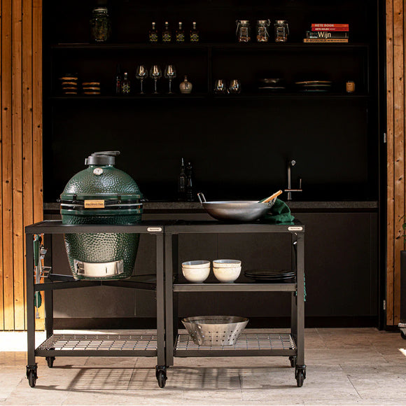 Outdoor kitchen setup with a large green grill on a cart, shelves with cookware in the background.